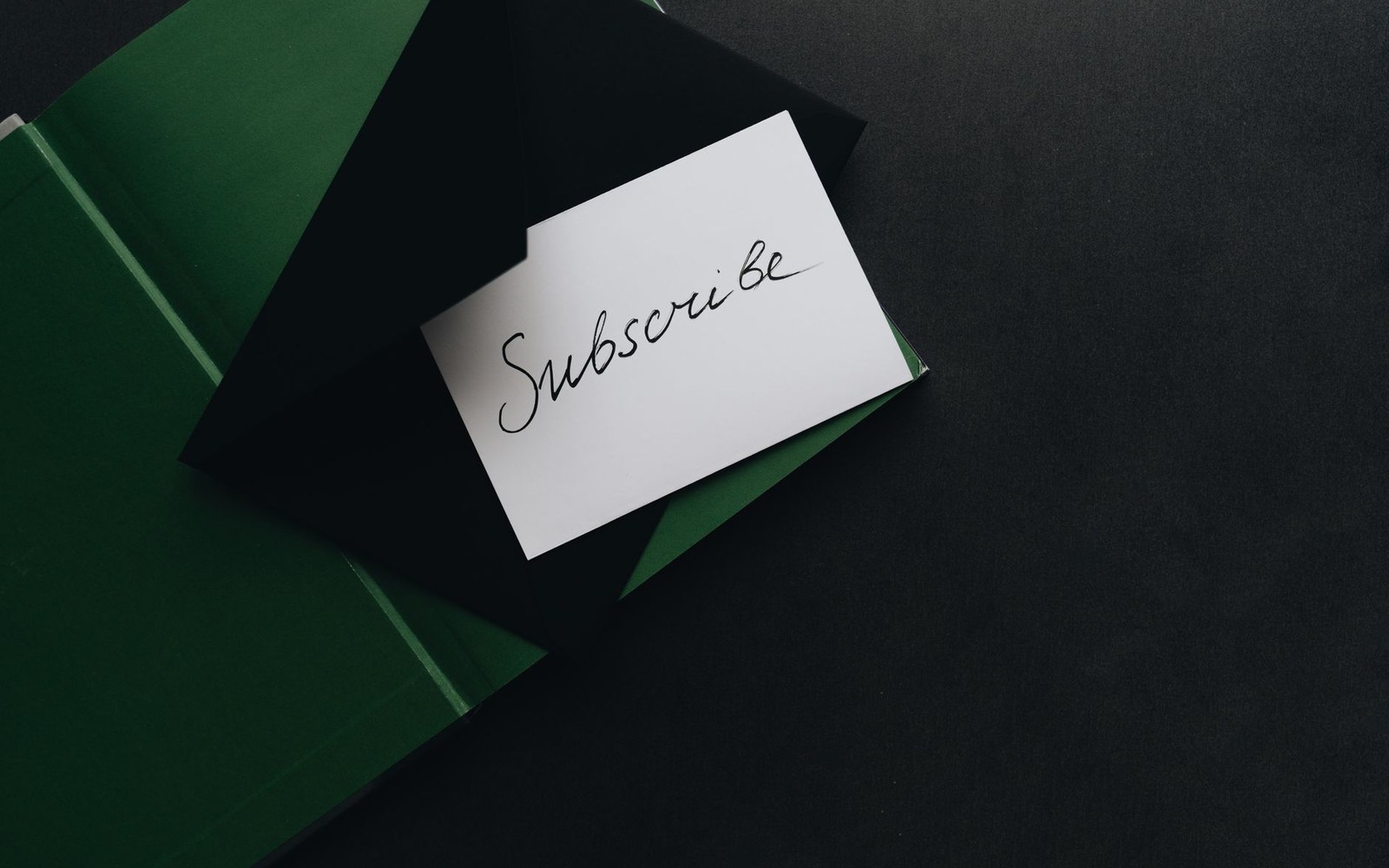 A white card reading "subscribe" placed on an open black and green envelope